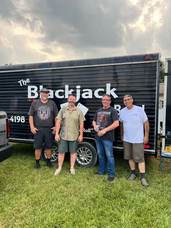 Four members of The Blackjack Band standing in front of their black band trailer