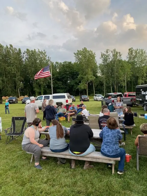 Families seated at picnic tables on the lawn with an American flag flying behind them