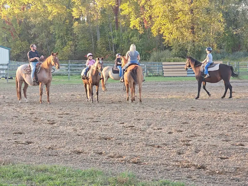 Young riders on horseback lined up in the outdoor arena with an instructor