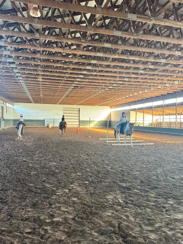 Wide view of the indoor arena with riders and a small jump set up