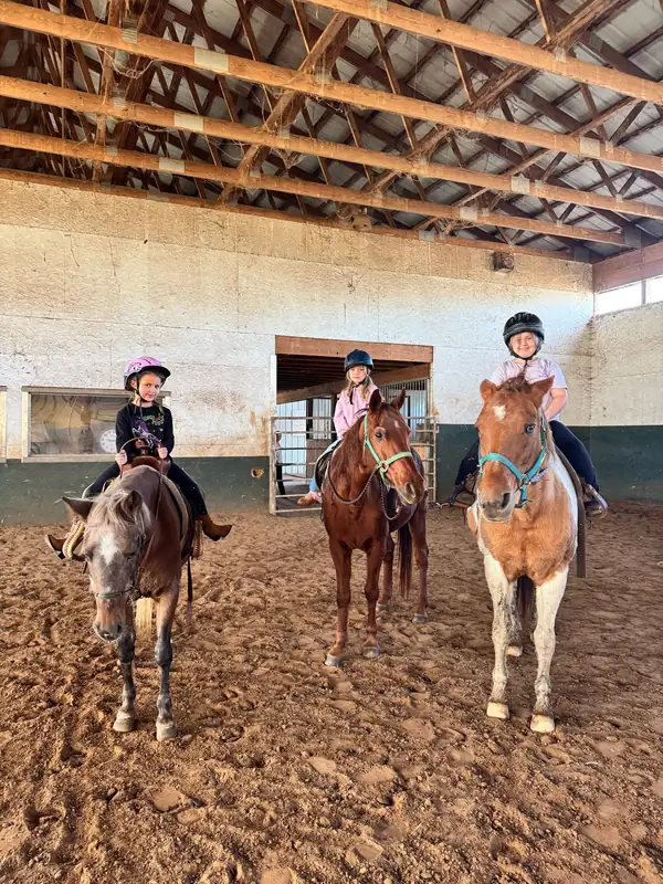 Three young riders in helmets on horses in the indoor arena